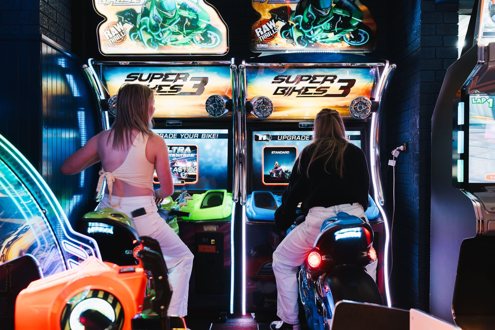 Two People Playing Motorcycle Arcade Racing Games in a Neon-lit Arcade — Orange Tenpin Bowl in Orange, NSW
