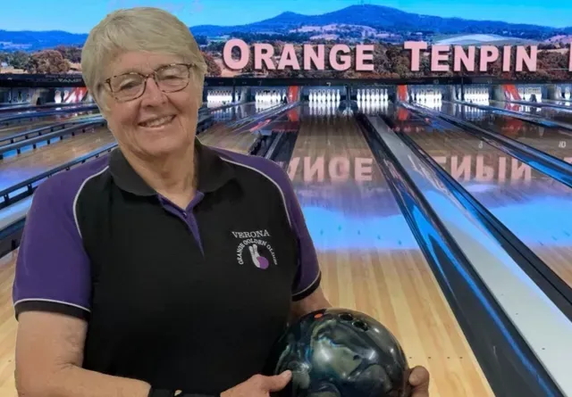 Person holding a bowling ball at Orange Tenpin lanes, smiling in front of the bowling alley backdrop