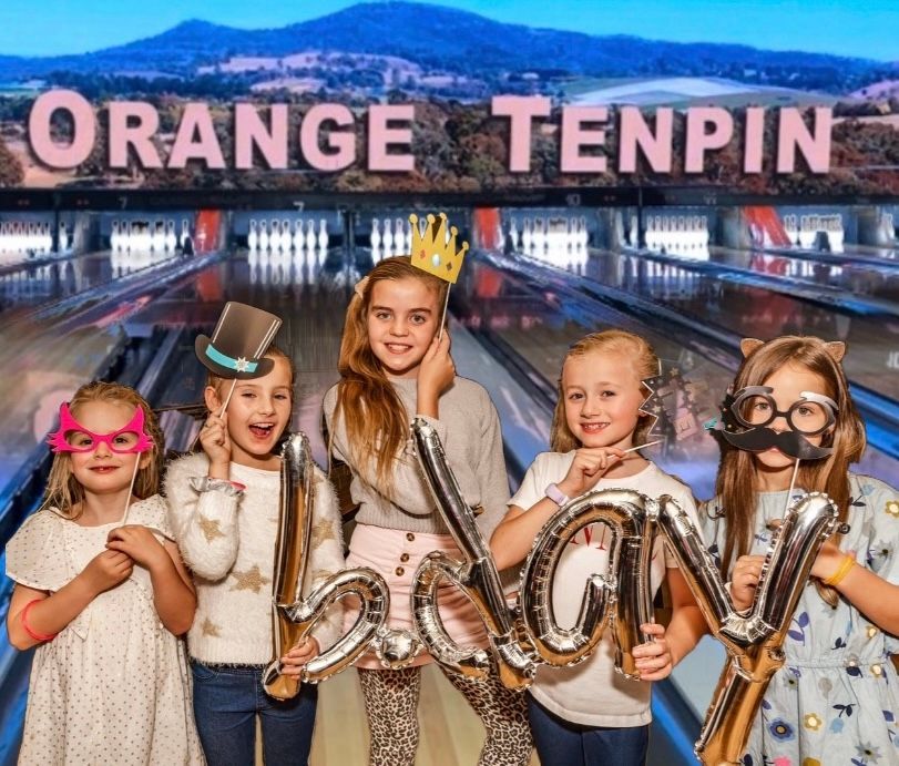 Five Children Holding Silver Balloons in Front of an Orange Tenpin Bowling Sign at Night — Orange Tenpin Bowl in Orange, NSW