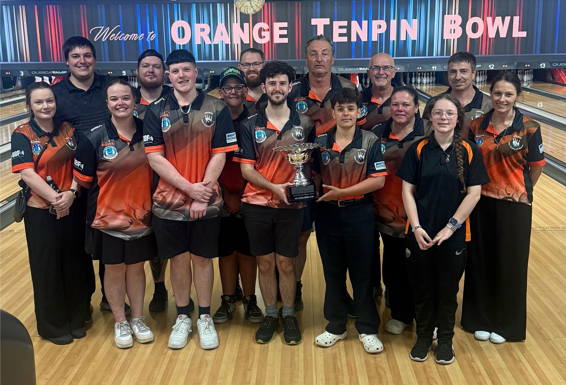 Team Group Photo With Trophy at Orange Tenpin Bowl, Wearing Black and Orange Uniforms — Orange Tenpin Bowl in Orange, NSW
