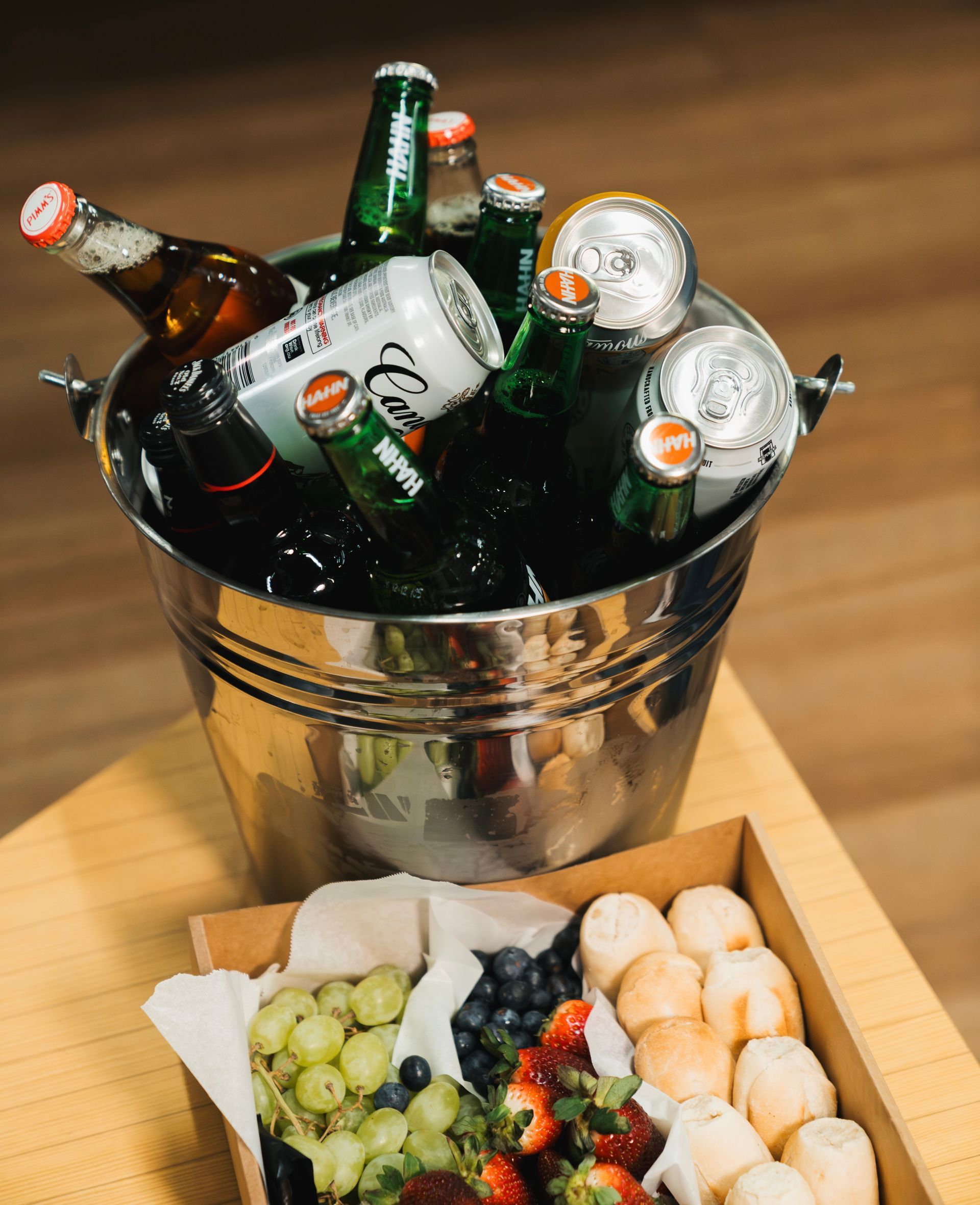 Ice bucket with chilled beer bottles beside a tray of grapes, strawberries, and pastries on a table