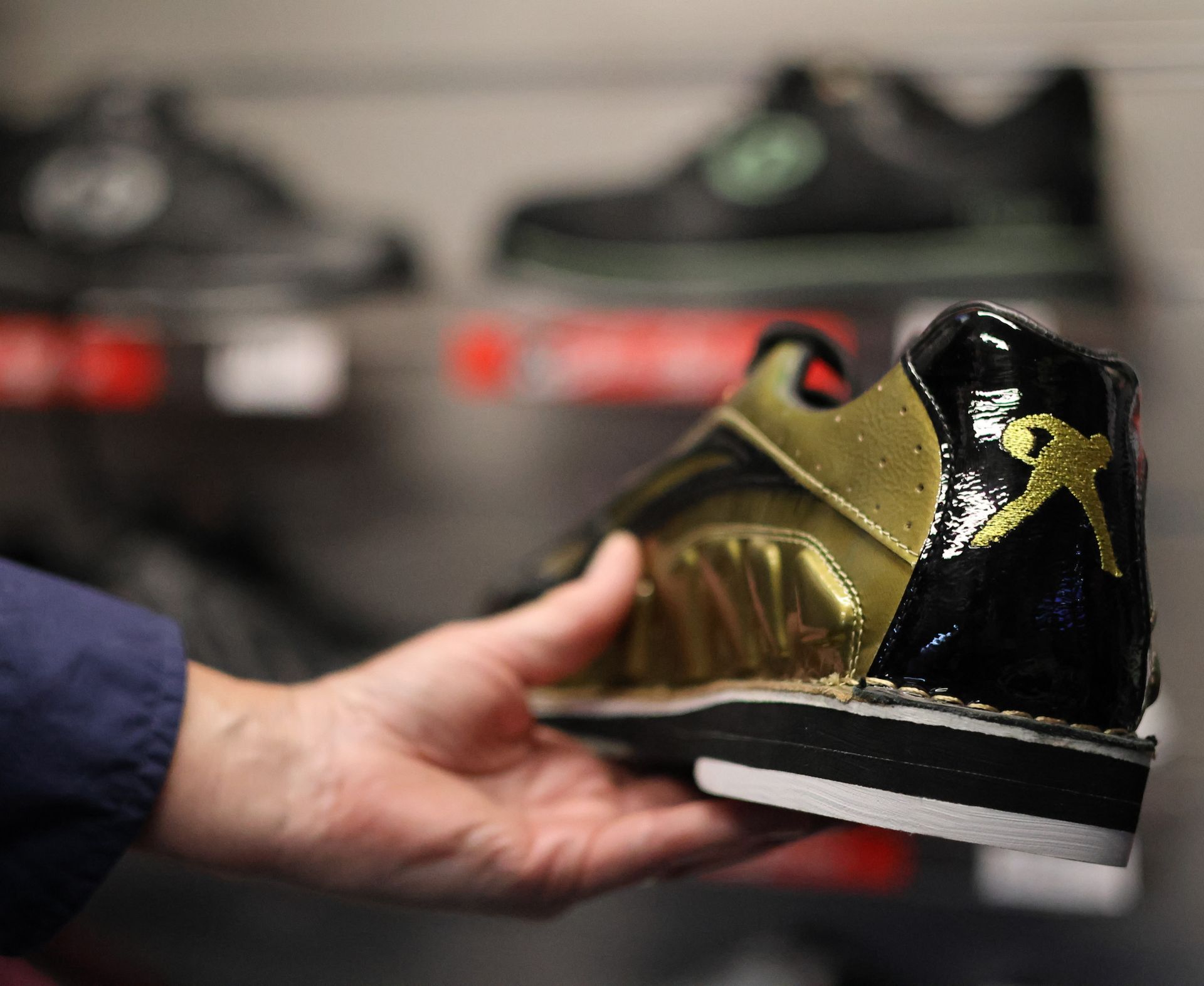 Hand Holding a Black-and-gold Sneaker With a Red Accent in Front of Blurred Shoes — Orange Tenpin Bowl in Orange, NSW