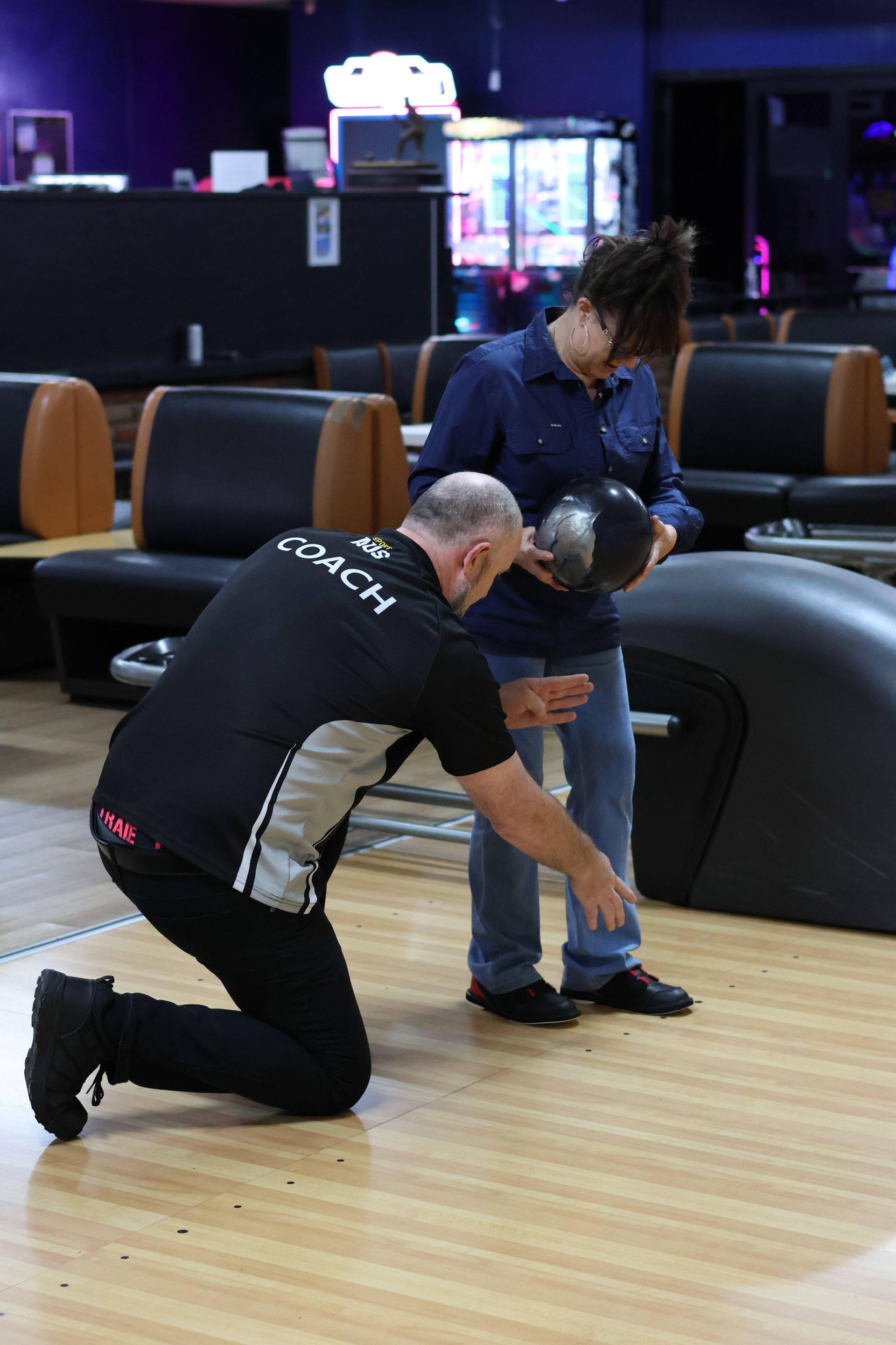 Man Kneels to Adjust a Seated Person's Shoe in a Bowling Alley Lane Area — Orange Tenpin Bowl in Orange, NSW