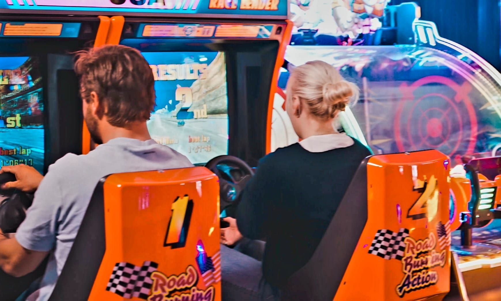 Two People Seated in Orange Arcade Racing Game Chairs, Facing a Bright Game Screen — Orange Tenpin Bowl in Orange, NSW