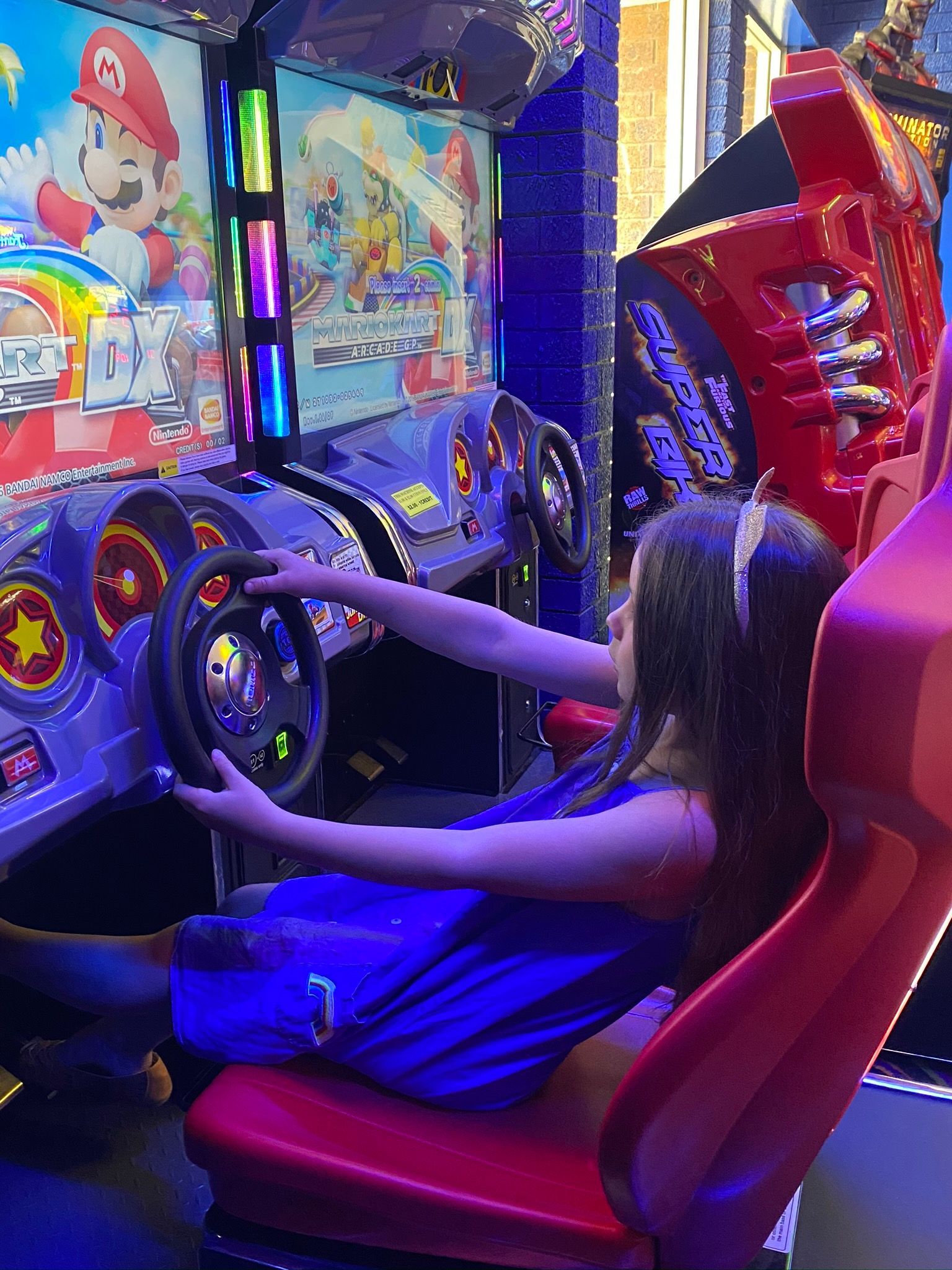 Person Playing a Arcade Racing Game, Seated in a Red Chair Under Neon Lights. — Orange Tenpin Bowl in Orange, NSW