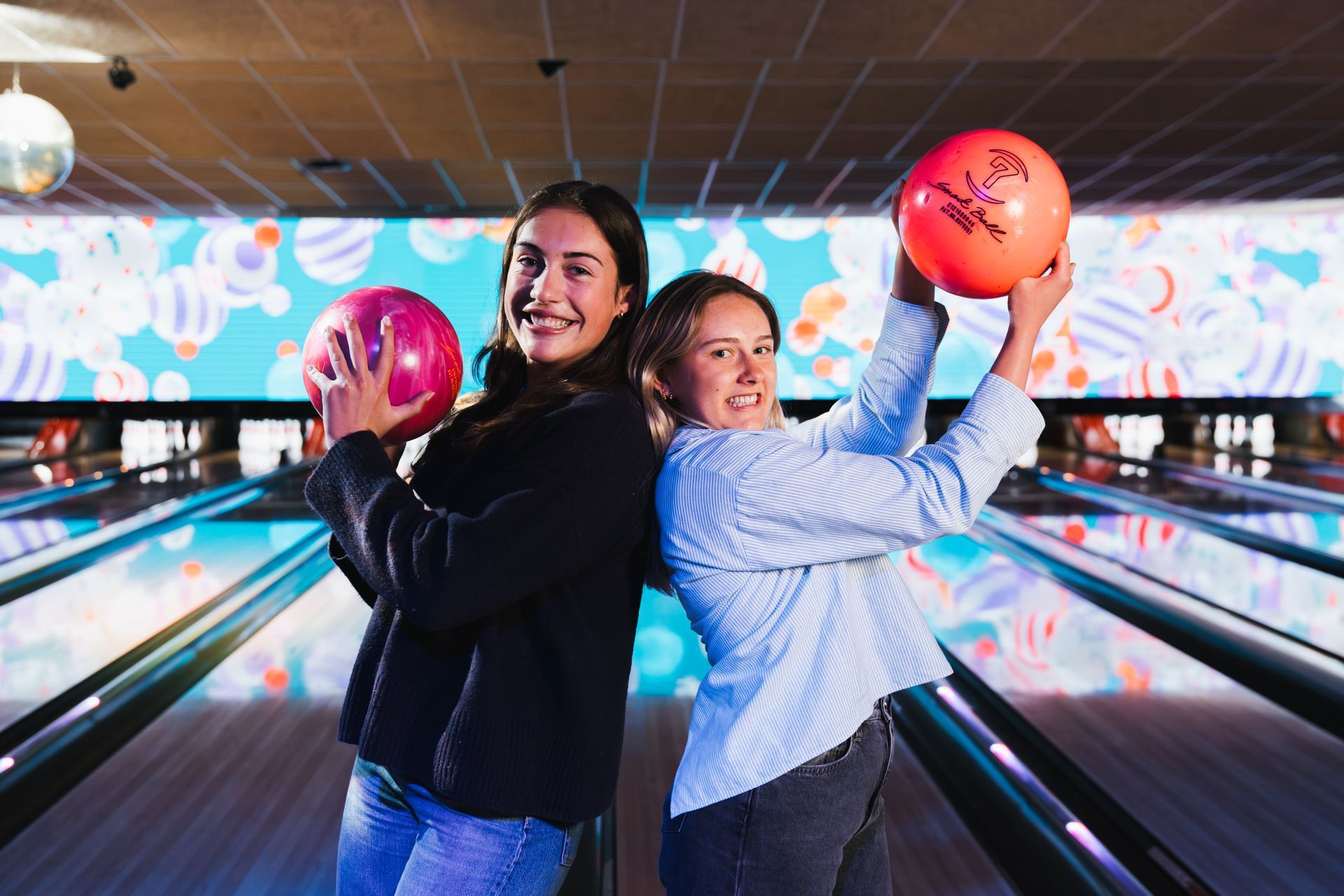 Two People Smiling and Posing With Bowling Balls in a Brightly Lit Bowling Alley — Orange Tenpin Bowl in Orange, NSW