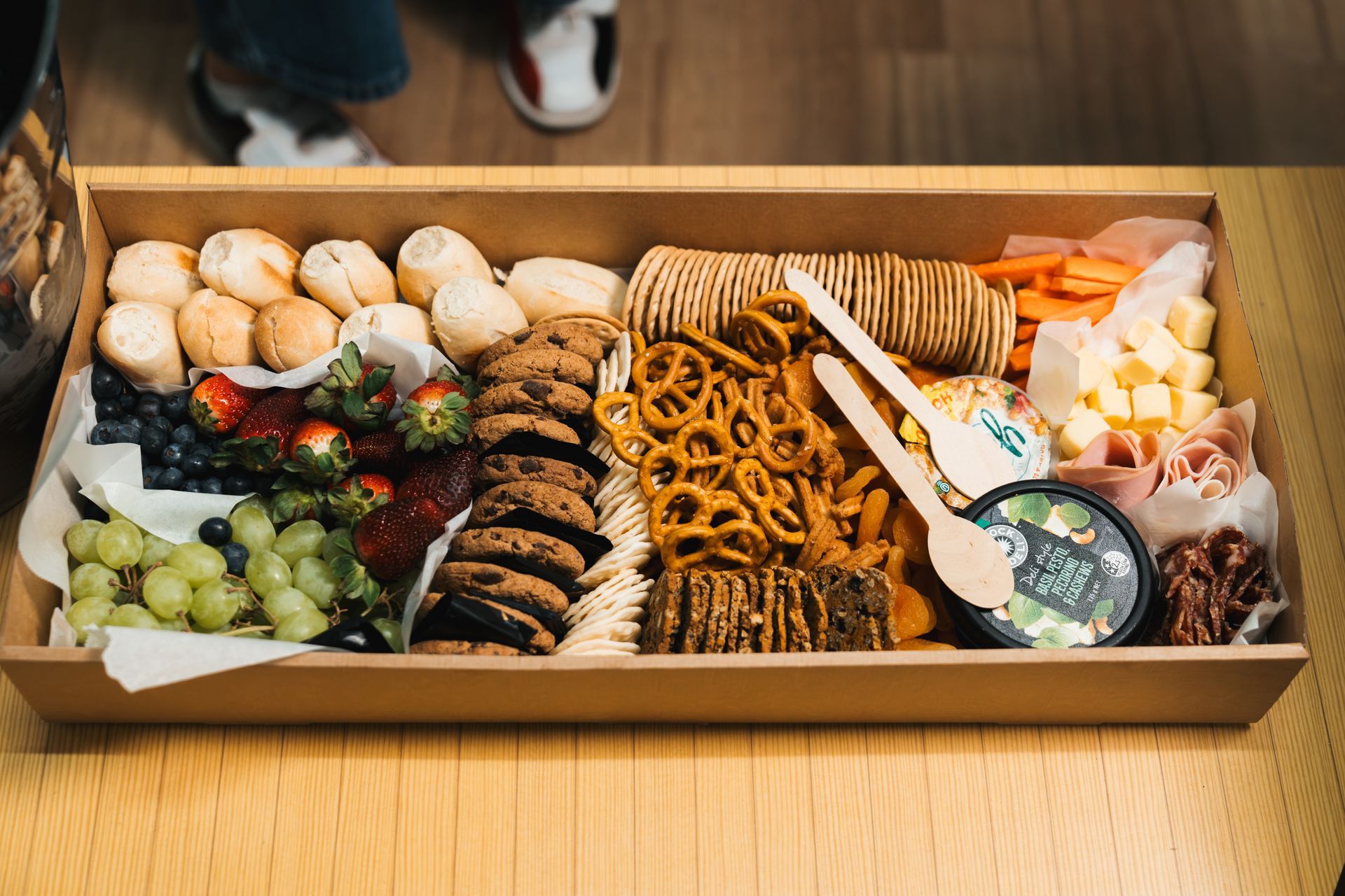 Assorted appetizer platter with pastries, pretzels, grapes, crackers, and dip in a wooden box