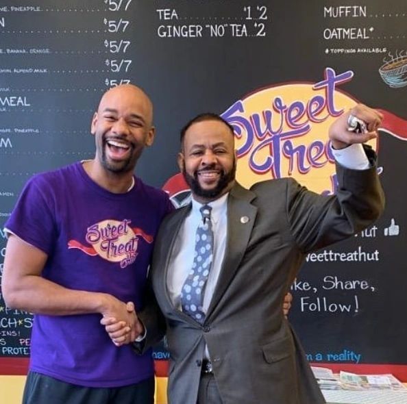 Two men standing in front of a sign that says sweet treat