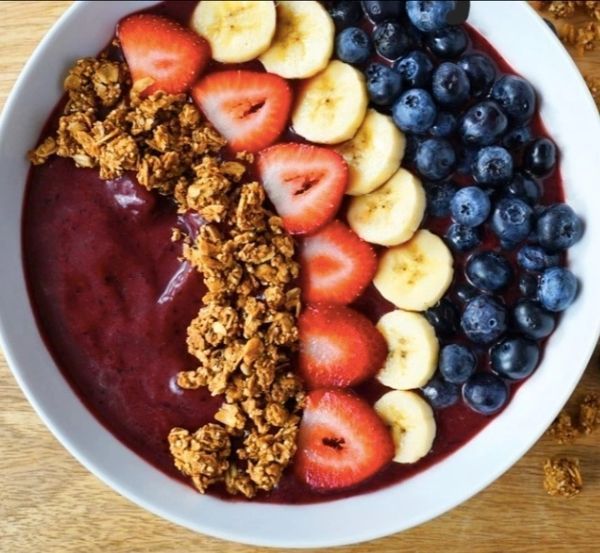 A bowl filled with strawberries bananas blueberries and granola