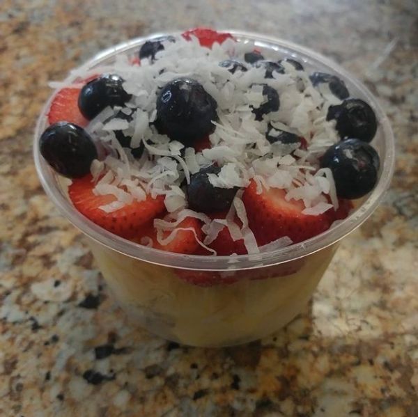 A plastic cup filled with strawberries blueberries and shredded coconut