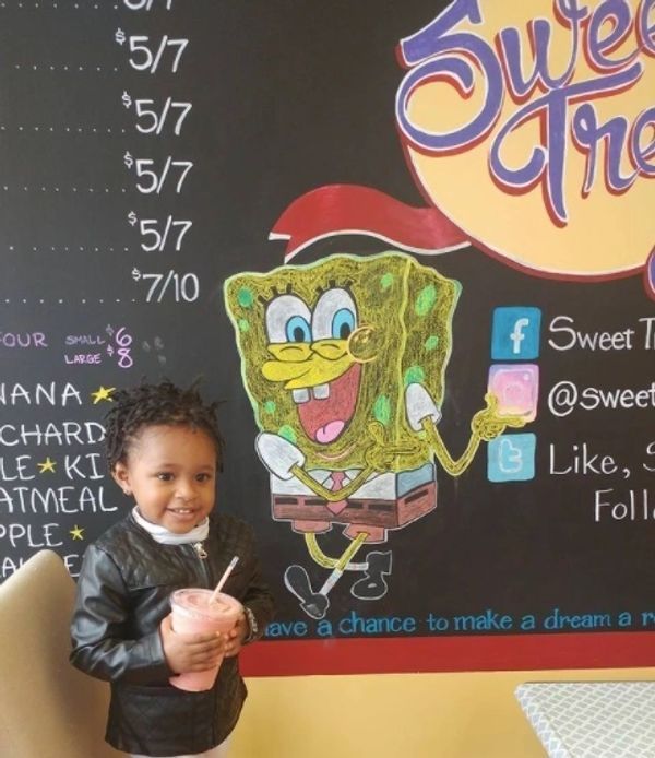 A little girl stands in front of a chalkboard with spongebob on it