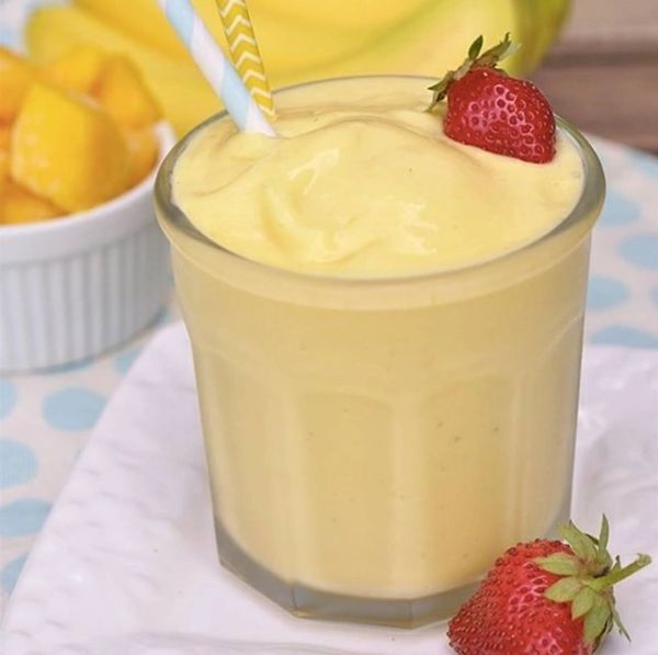 A yellow smoothie with a straw and a strawberry on top