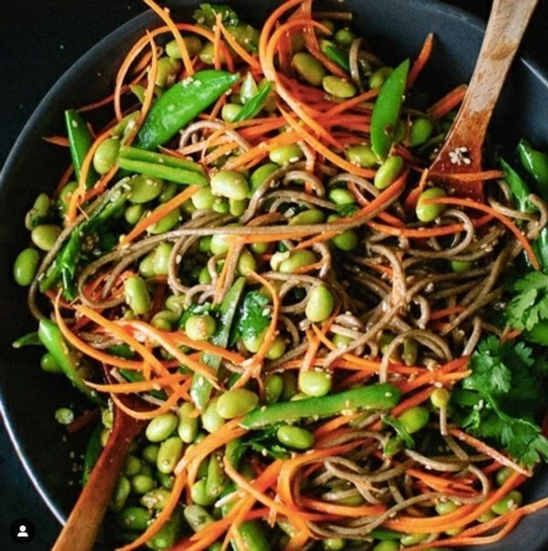 A bowl of noodles and vegetables with a wooden spoon
