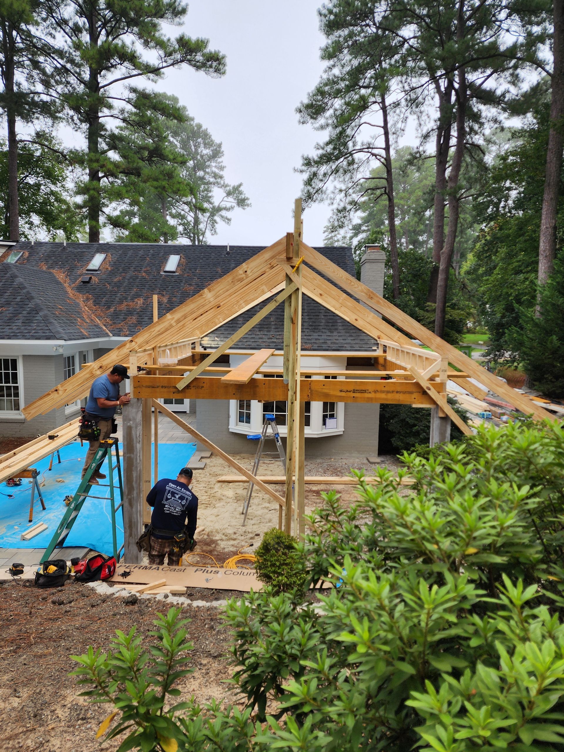 Two construction workers building a wooden roof structure extension on a house, cloudy day.