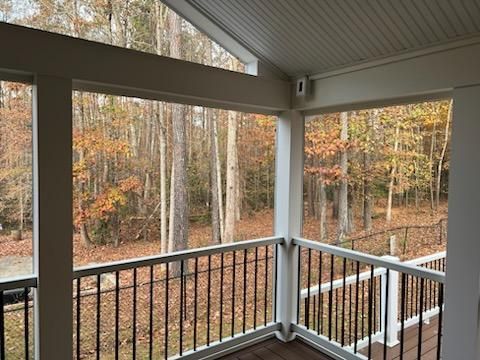 Covered porch with black railing, white columns, overlooking autumn trees.