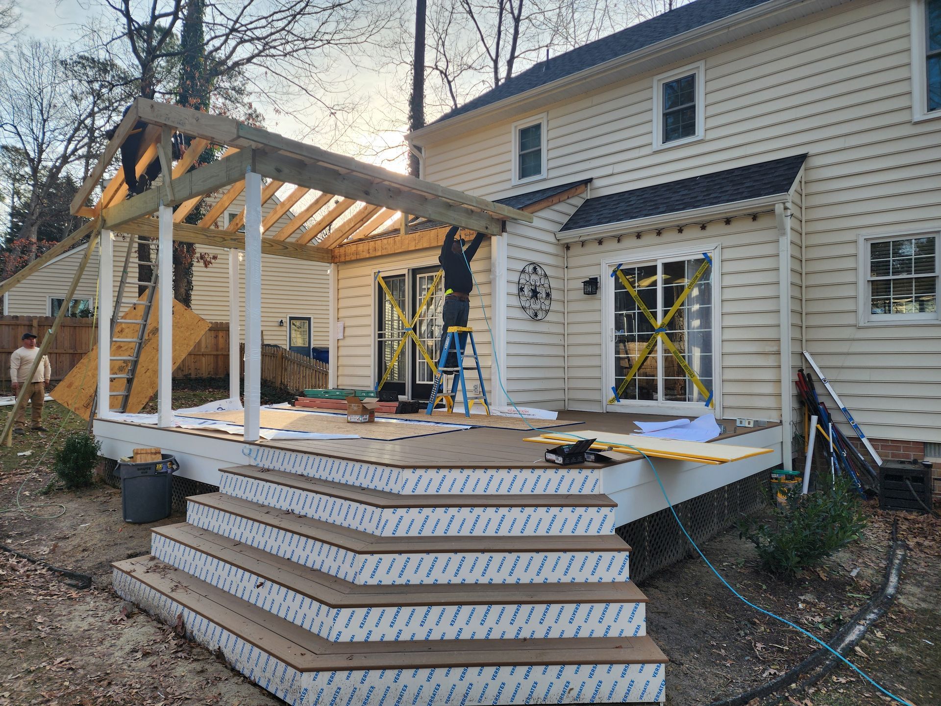 Deck construction: Men building a covered porch attached to a two-story beige house.