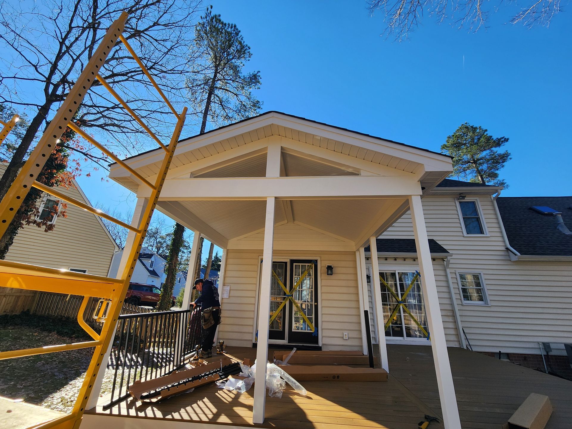 A newly built, white-trimmed covered patio extension on the back of a beige house under a clear sky.
