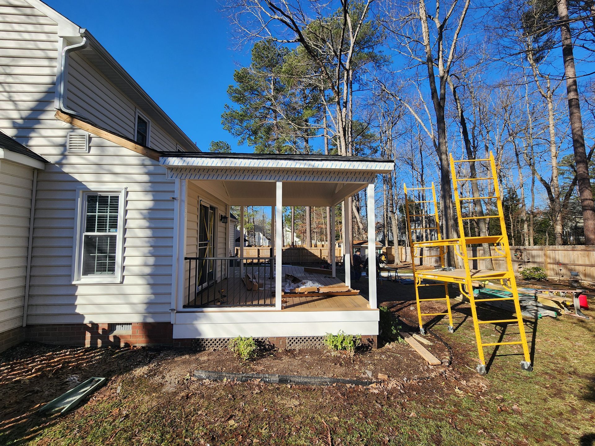 A partially constructed porch on a house; yellow ladder, white siding, clear blue sky.