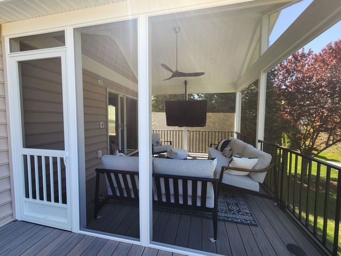 Screened porch with white trim, couch, TV, and ceiling fan; dog on right; sunny day.