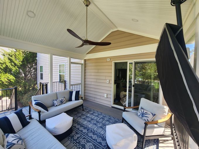 Screened-in porch with gray sofas, blue rug, ceiling fan. Sliding glass door leads inside.