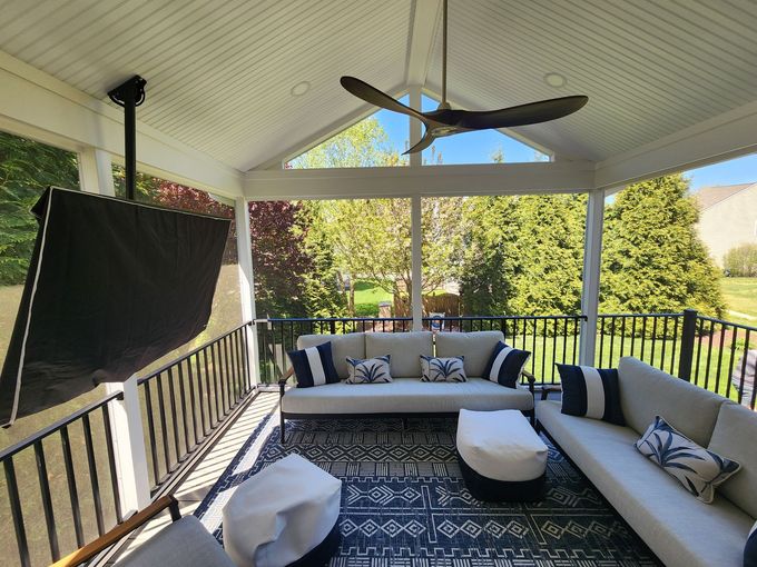 Screened-in porch with outdoor seating and a television. Lush trees are visible through the screens.