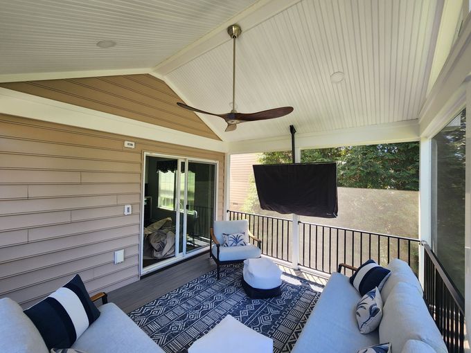 Covered patio with white furniture, blue rug, TV, and ceiling fan.