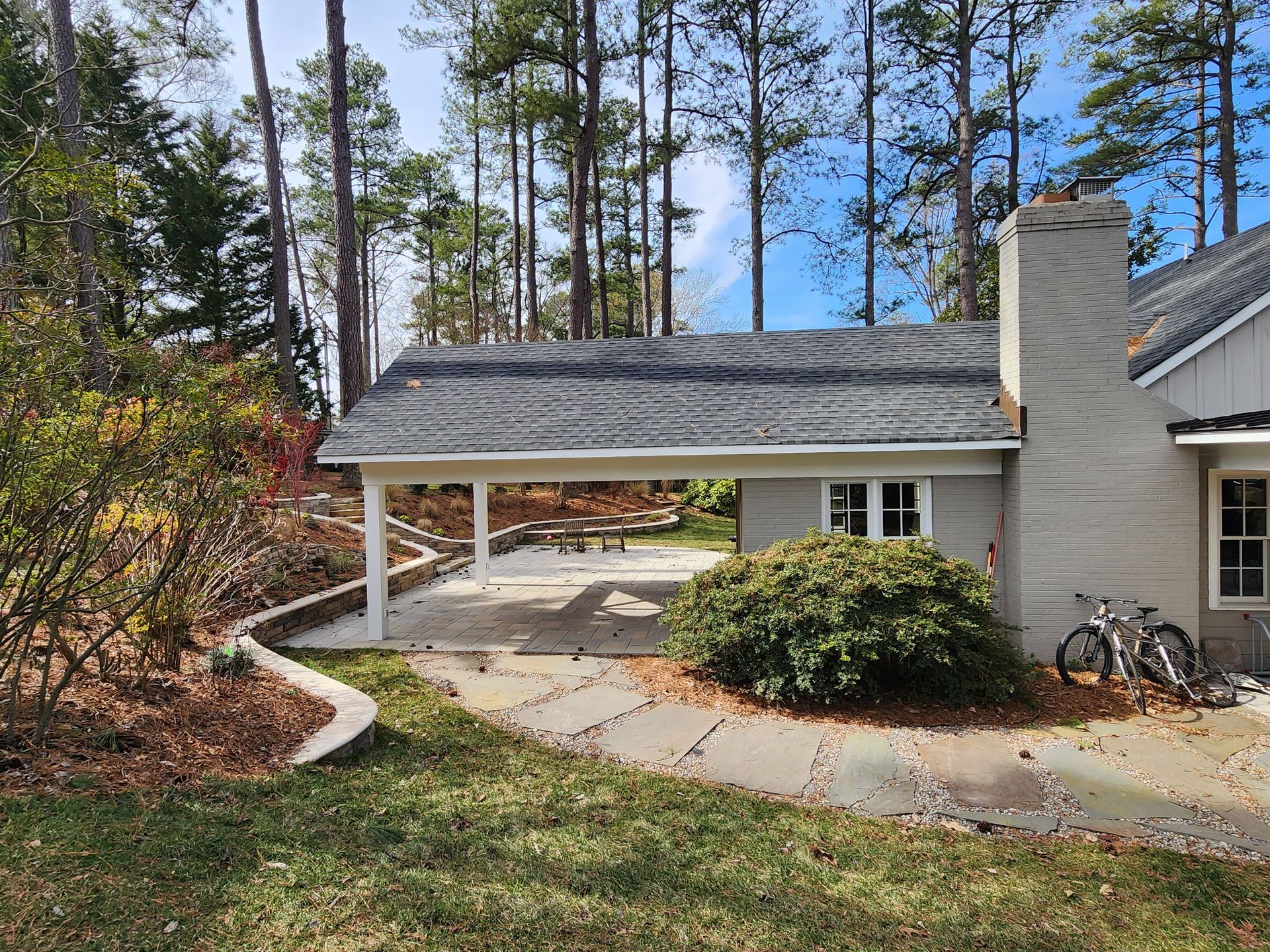 A covered patio with a chimney, next to a gray building and trees. Two bikes lean on the building.