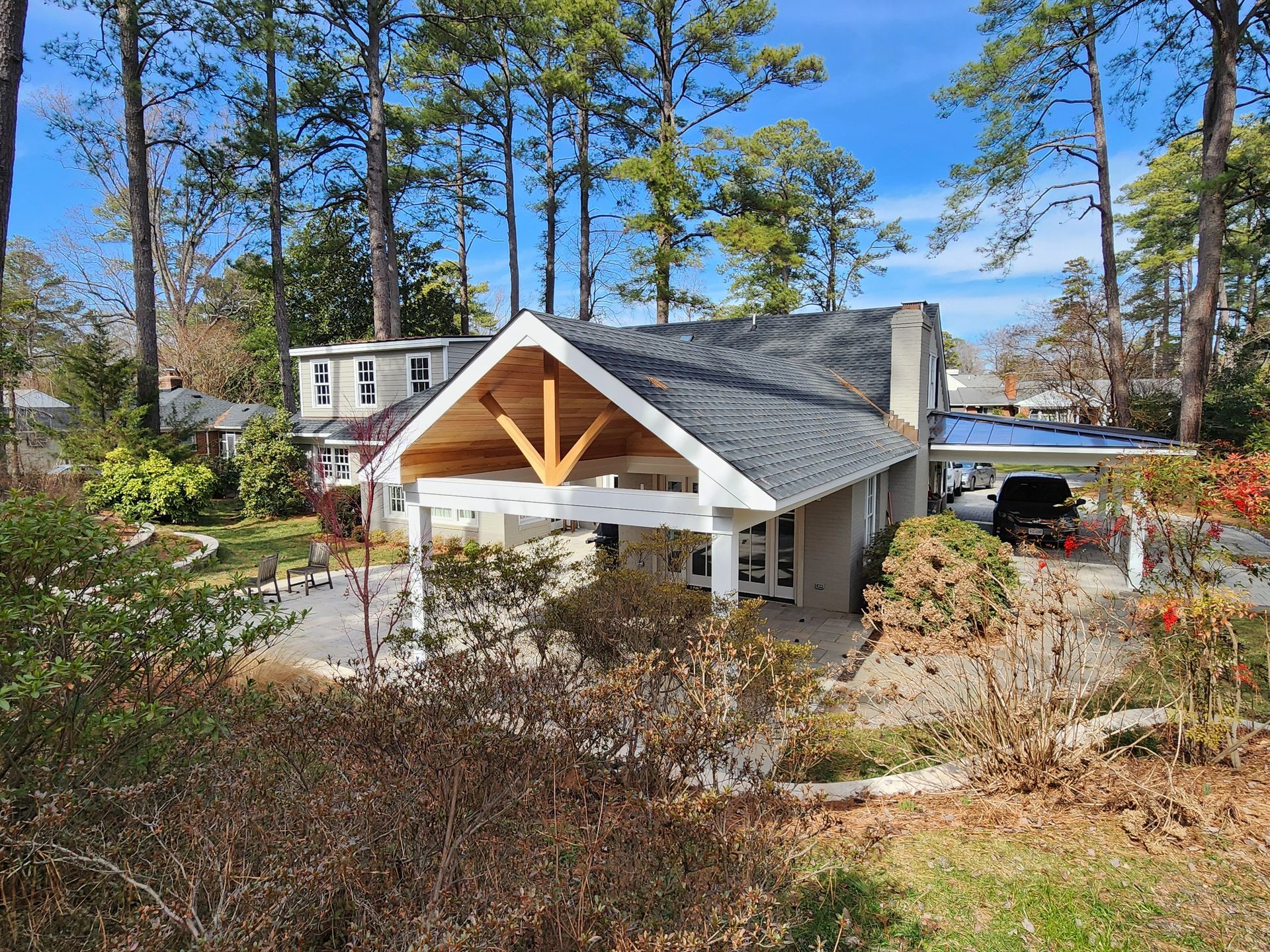 House with white accents, carport, and a car parked under it, surrounded by trees and foliage.