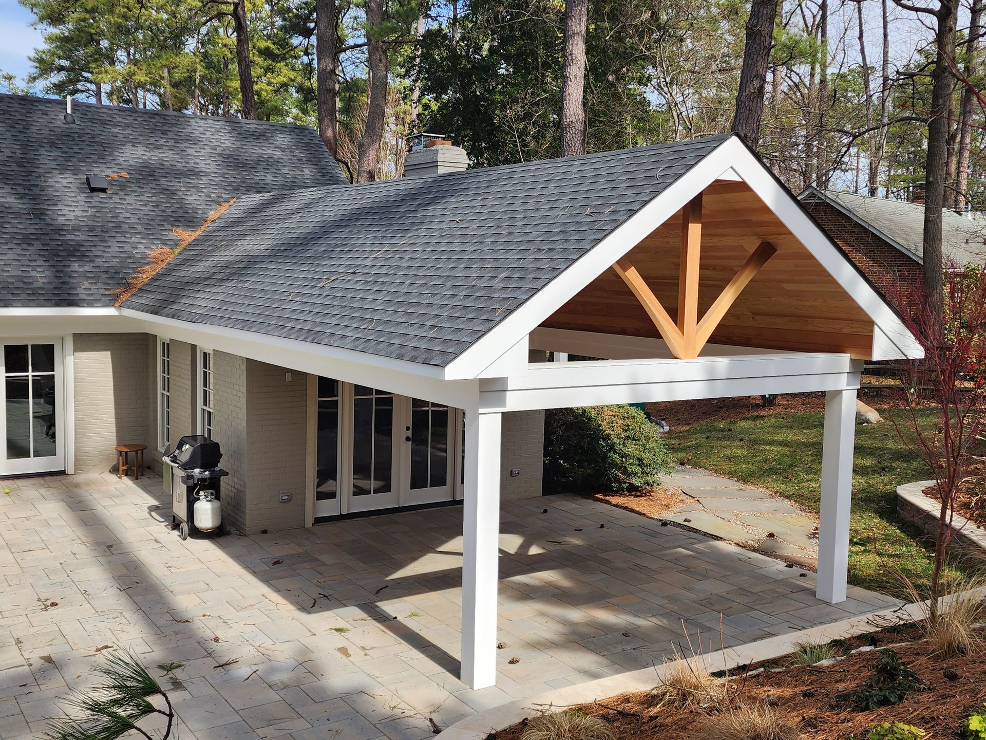 White-columned covered patio attached to a house with a gray roof. A wooden beam is visible.