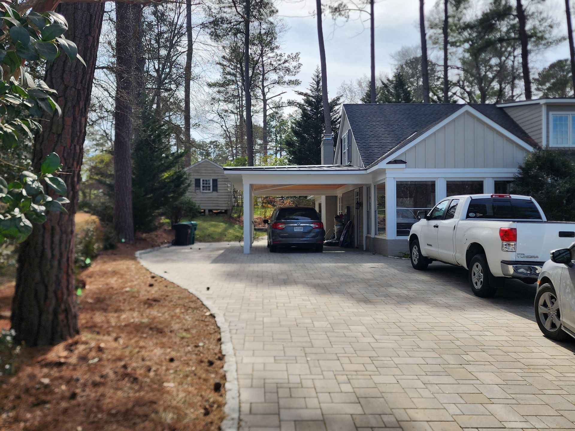 Driveway of a house with a car and carport. White truck parked to the right.