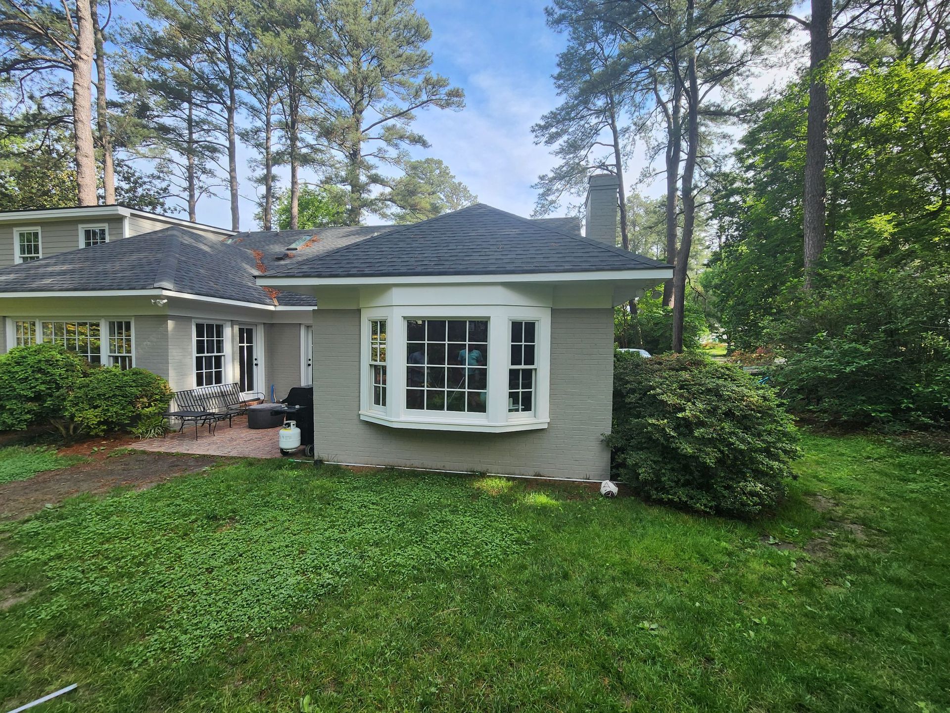 Tan house with a bay window, dark roof, chimney, and lush green surroundings.