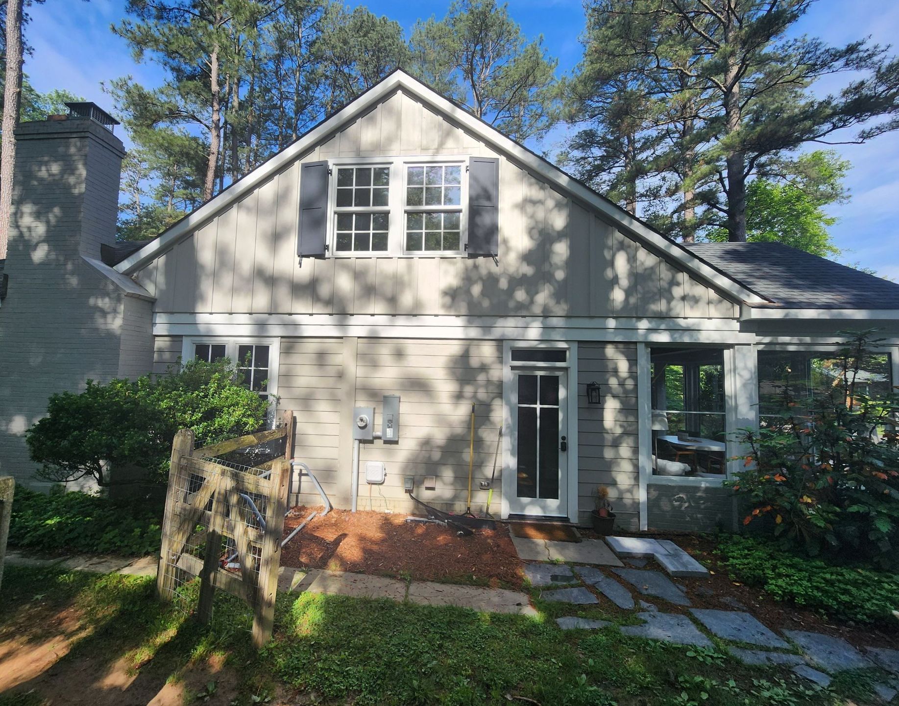 Gray house with black shutters, door, and chimney. Blue sky, trees, and stone walkway.