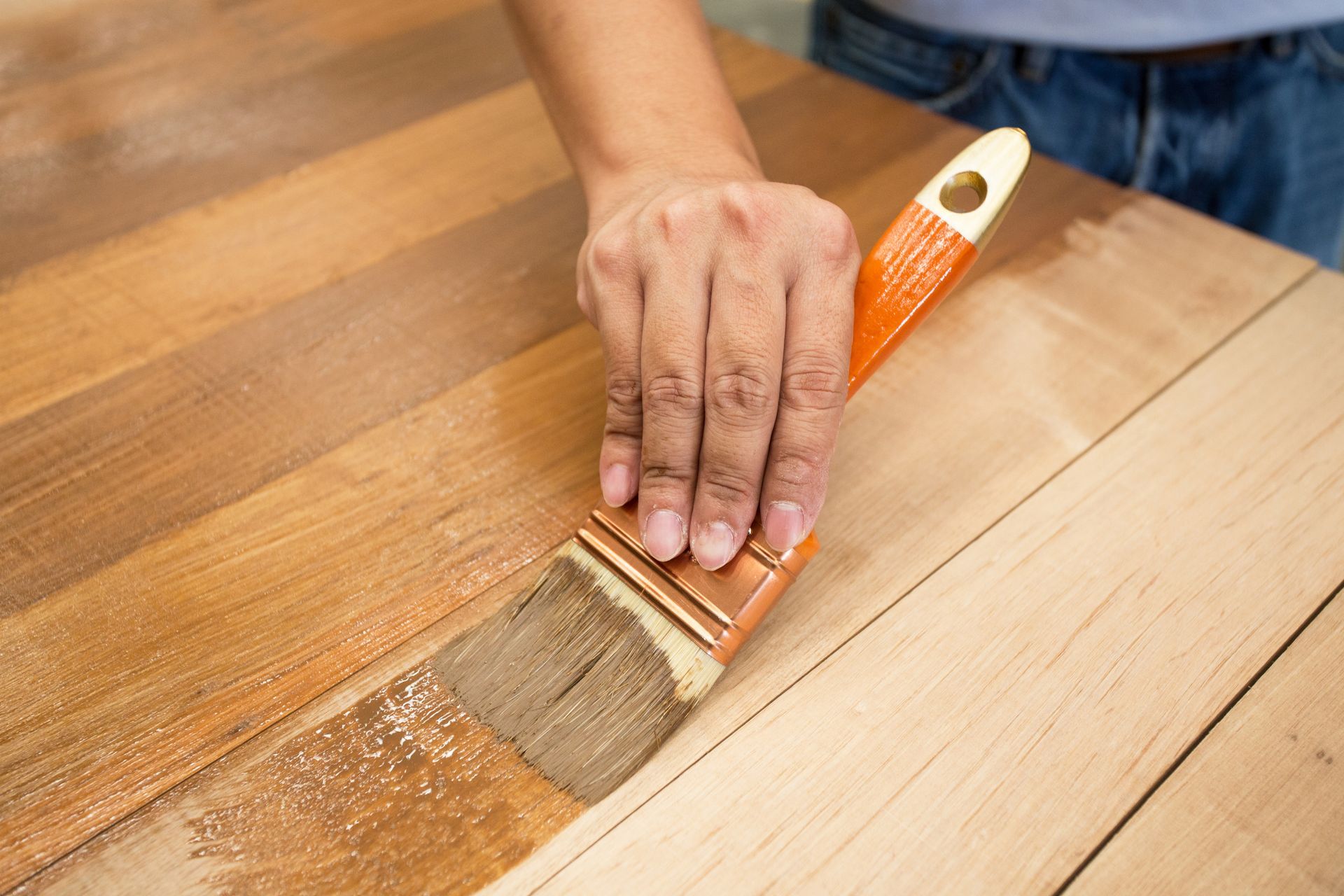 Hand applying wood varnish with brush on wooden surface for smooth finish.