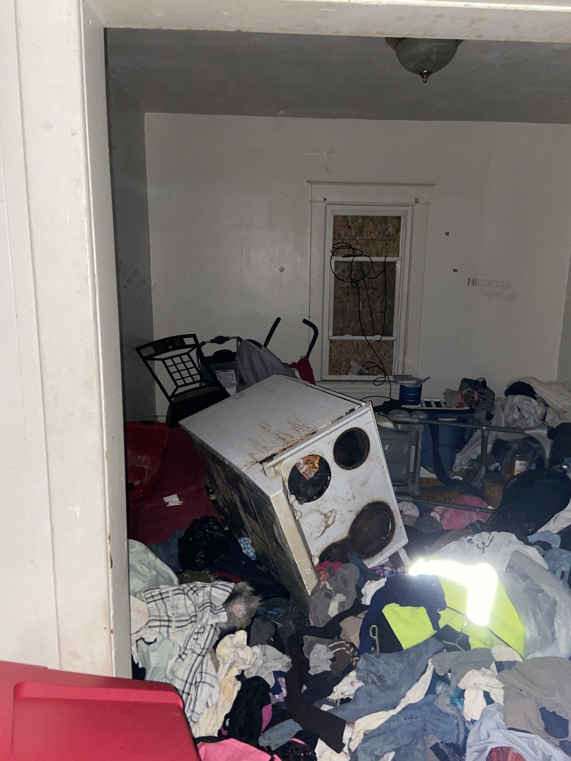 Flooded room with a tipped washer, scattered clothes, and debris piled across the floor.