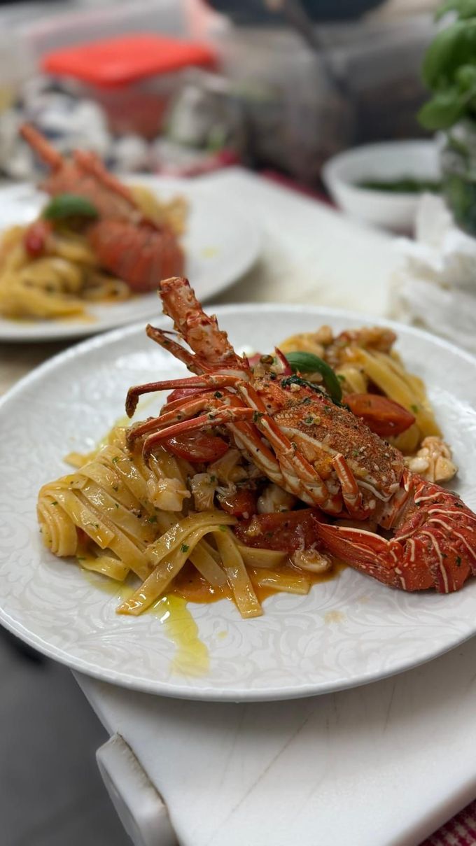 Un piatto di pasta all'astice su un tavolo bianco, con un secondo piatto, sfocato, sullo sfondo.
