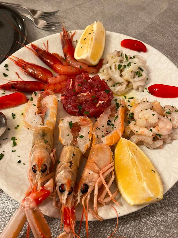 Piatto di frutti di mare con gamberi, scampi, ostriche, spicchi di limone e salsa rossa su un piatto bianco.