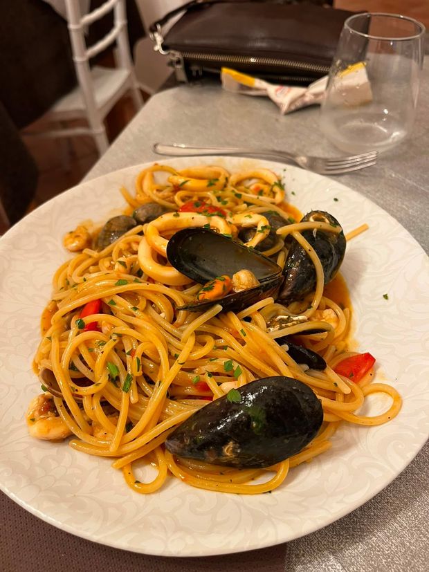 Piatto di spaghetti con cozze e peperoni rossi su un tavolo di ristorante.