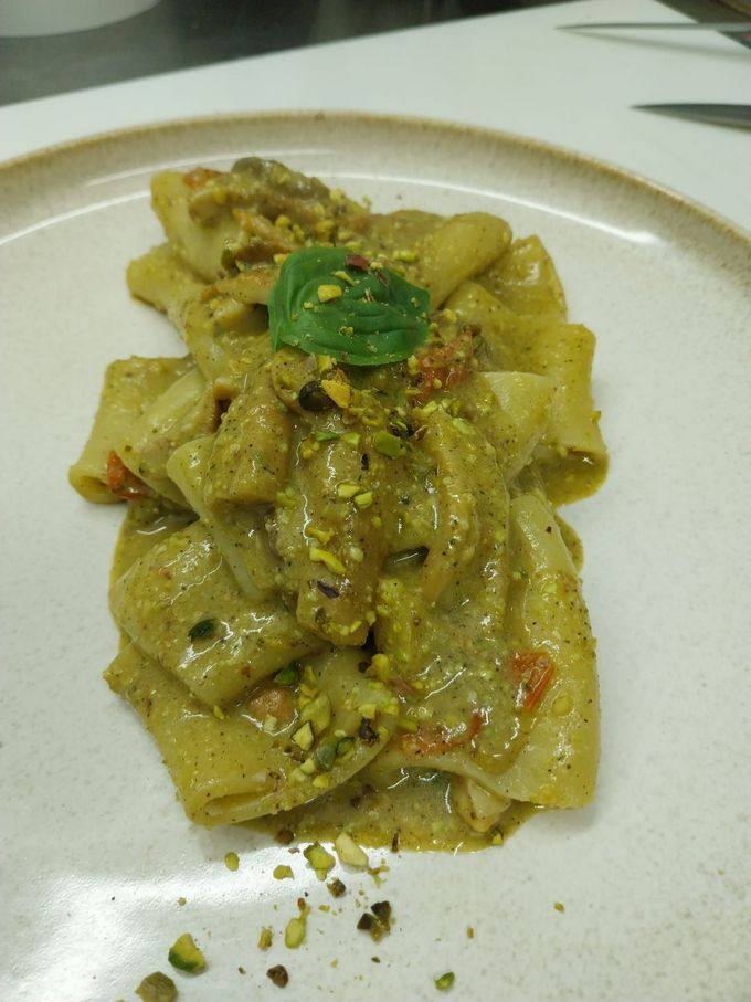 Pasta cremosa con erbe aromatiche e pistacchi tritati su un piatto bianco.