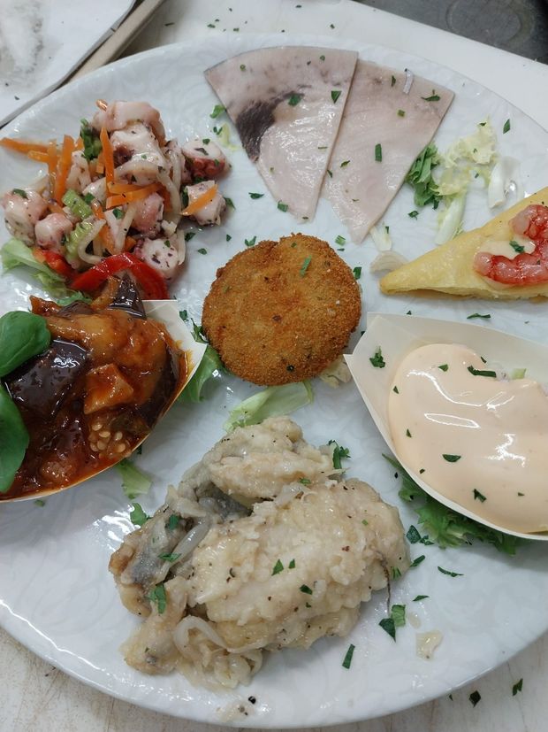 Antipasti assortiti su un piatto bianco, tra cui salse, insalata, fette di pane e una crocchetta.