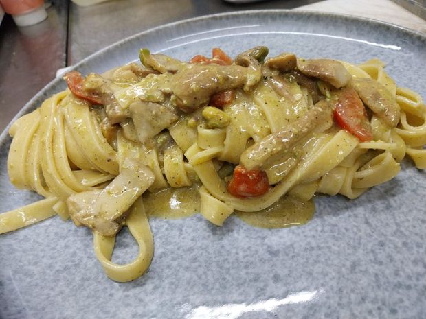 Fettuccine cremose con pollo e peperone rosso servite su un piatto.