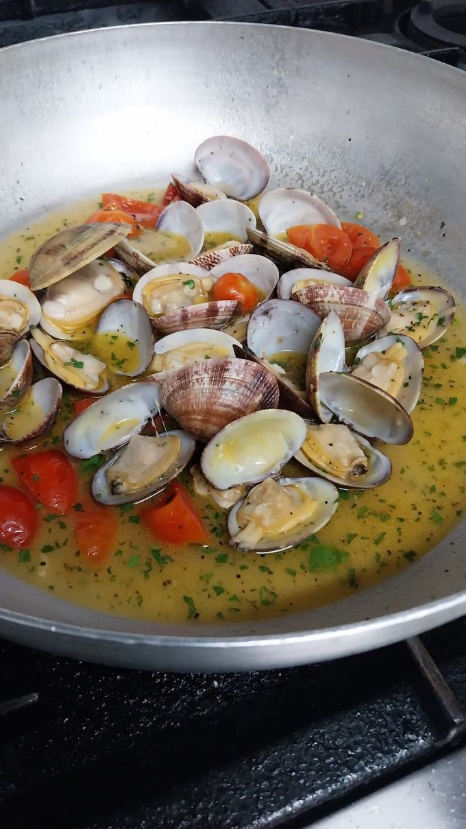 Vongole e pomodorini che sobbollono in un brodo giallo in una padella sul fornello