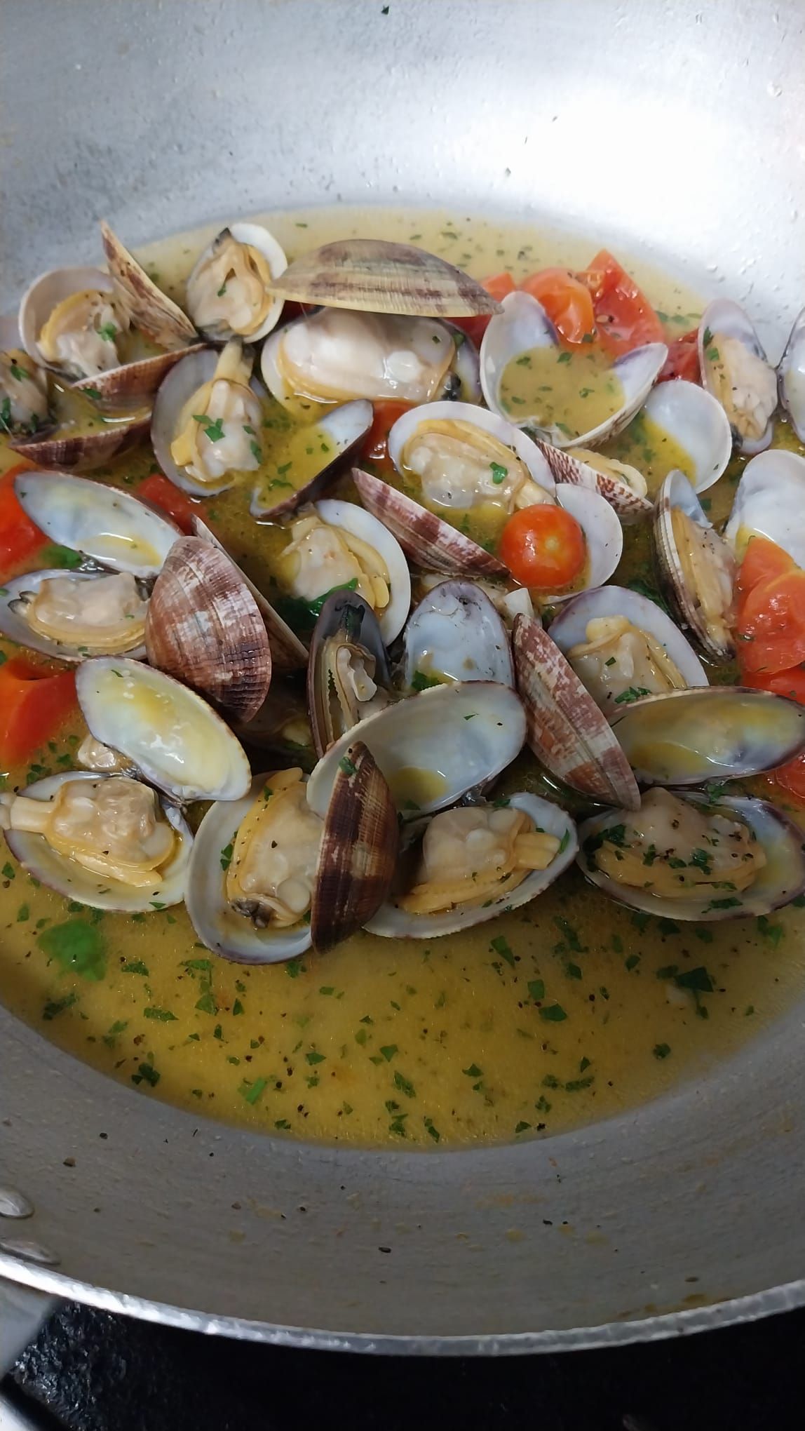 Vongole che sobbollono in padella con aglio, erbe aromatiche e pomodorini in brodo