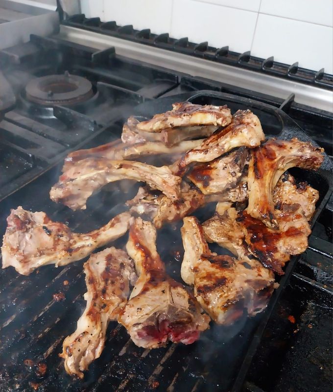 Carne grigliata che sfrigola sul piano cottura, con pezzi carbonizzati e fumo che sale dai fornelli.