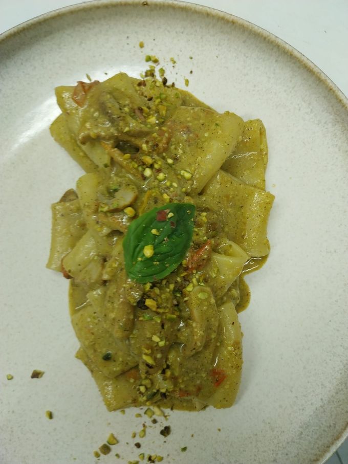 Pasta in salsa cremosa su un piatto bianco, guarnita con basilico e pistacchi tritati.