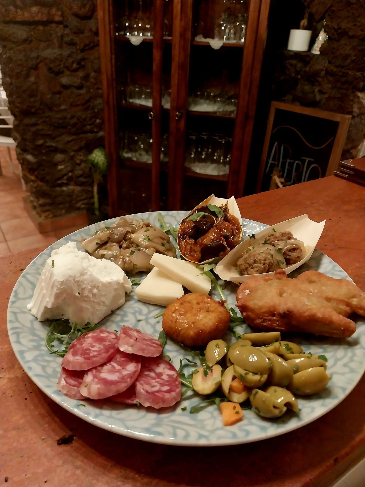 Un assortimento di piatti mediterranei con riso, olive, funghi, crocchette e verdure a foglia verde, disposti su un tavolo bianco.