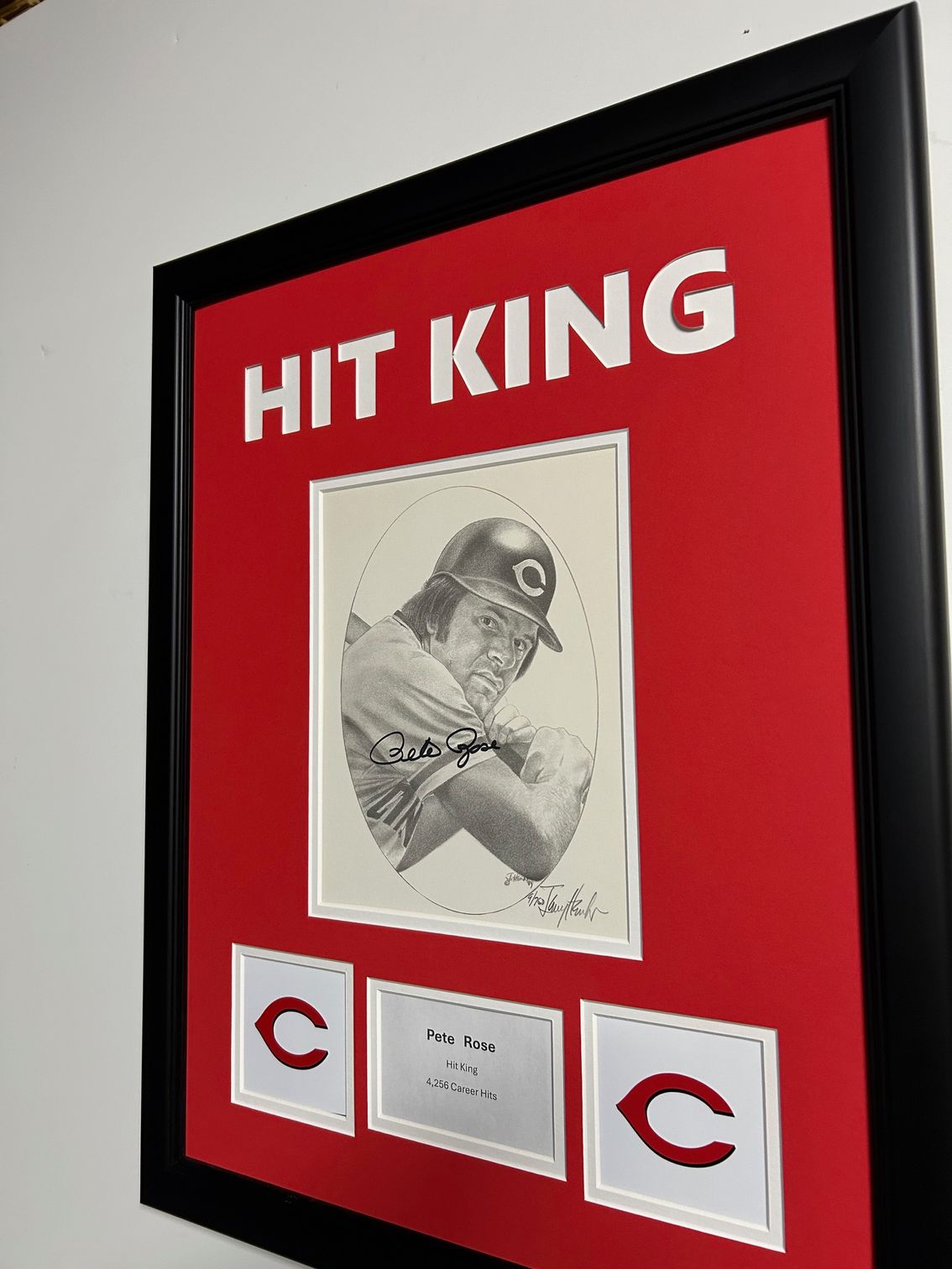 Framed black-and-red display with a sketch and two Cincinnati Reds logos around a center label