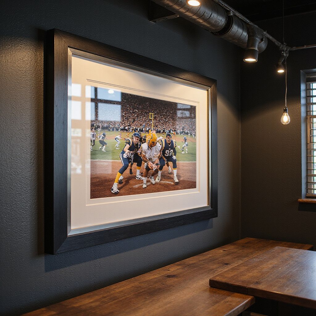 Framed baseball action photo on a dark wall above a wooden table in a dimly lit room