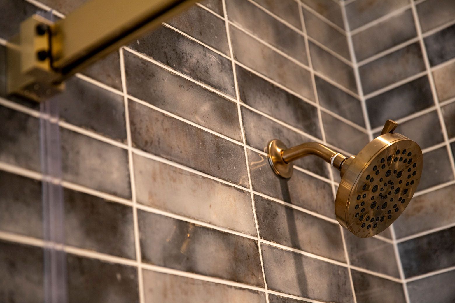 Close-up of a shower with unique wall tile and a gold shower head.