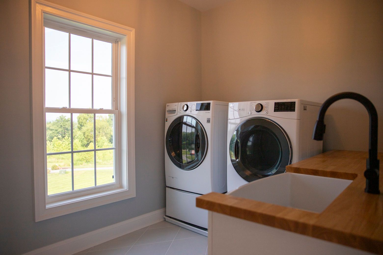 Laundry room remodel: wood butcher block counter, utility sink, and stacked washer/dryer near a window.
