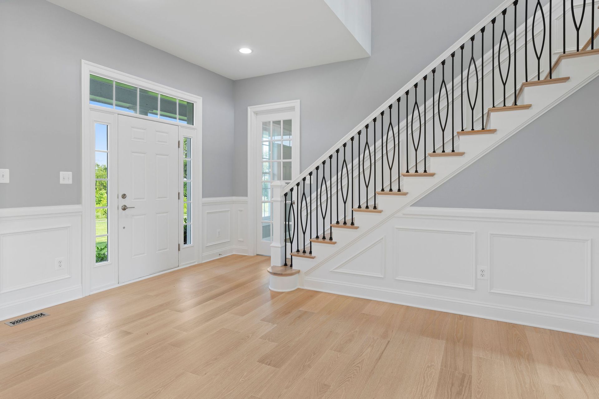 Foyer home entrance upgrade: custom staircase design, wainscoting, and modern front door installation.